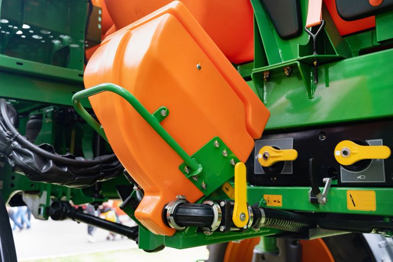 Close-up of vibrant orange and green agricultural machinery parts with yellow handles on a blurred outdoor background, emphasizing farming equipment