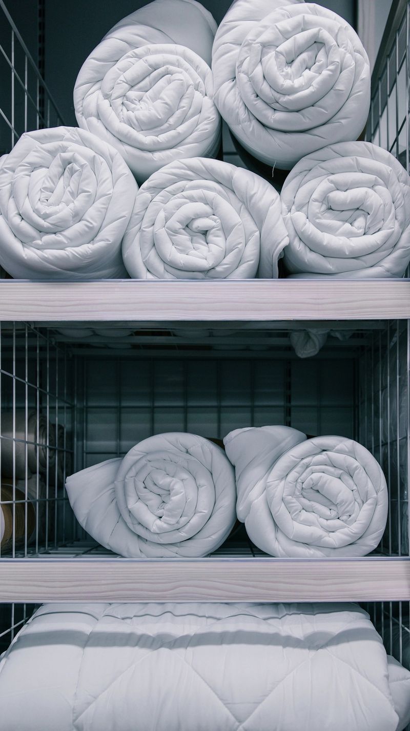 A retail display showcasing rolled bedding items, including duvets and comforters, organized on shelving units for sale
