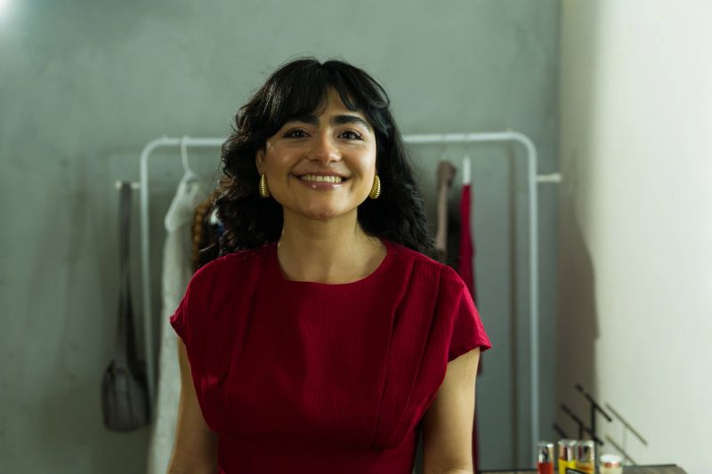Hispanic woman happily poses for the camera in a dressing room, surrounded by a clothing rack as she gets ready for a show or event
