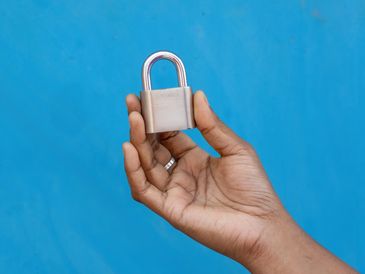 Hand holding a silver padlock against a blue background.