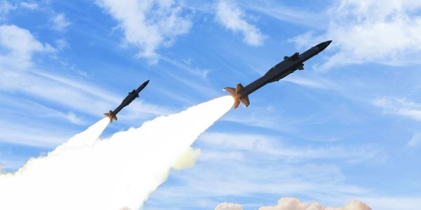 Two missiles launching into the sky against a blue sky with clouds.