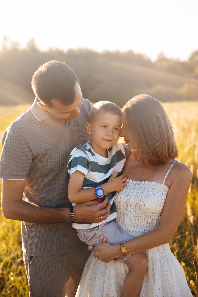 A family of three enjoys a sunny day in a golden field. The parents lovingly hold their young son, creating a warm and joyful atmosphere surrounded by nature.
