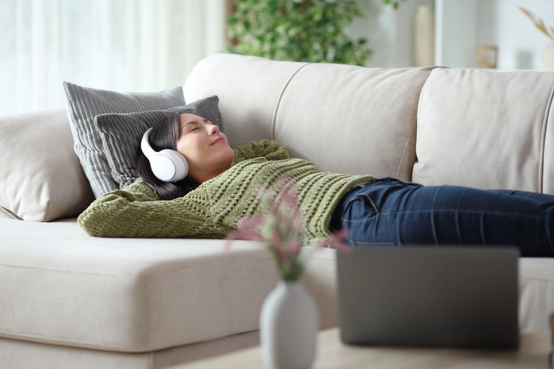 Asian woman wearing headphone lying on a couch listening audio therapies at home