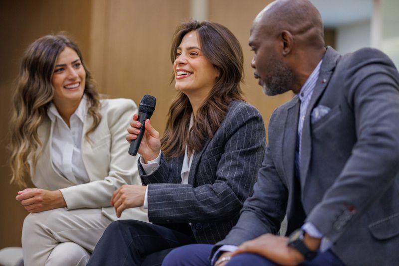 Diverse business professionals participating in panel discussion, woman speaking into microphone, sharing insights and smiling