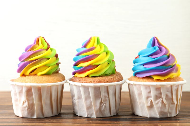 Delicious cupcakes with colorful cream on wooden table against white background, closeup