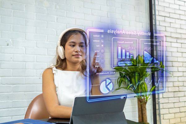 Woman analyzing futuristic sales data on a transparent digital screen with headphones on.