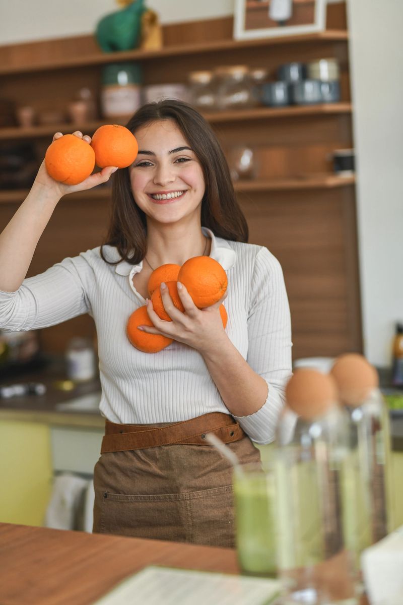 Smiling female barista holding oranges and striking a playful pose in a wellness-focused brunch cafe.