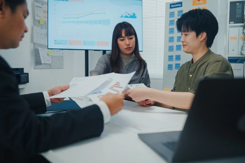 Young Asian business team meeting discusses market research findings and strategy in modern office. Planning, prioritization, strategic decision-making concept.