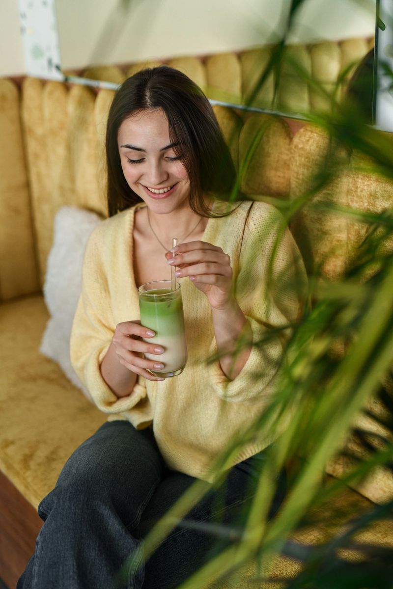 Smiling female guest sitting in a bright brunch cafe, enjoying matcha latte in natural light. Calm mood, leisure time, lifestyle concept.