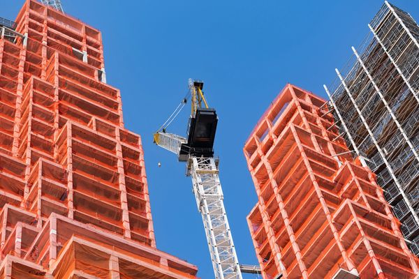 Construction site with crane and buildings covered in orange netting.