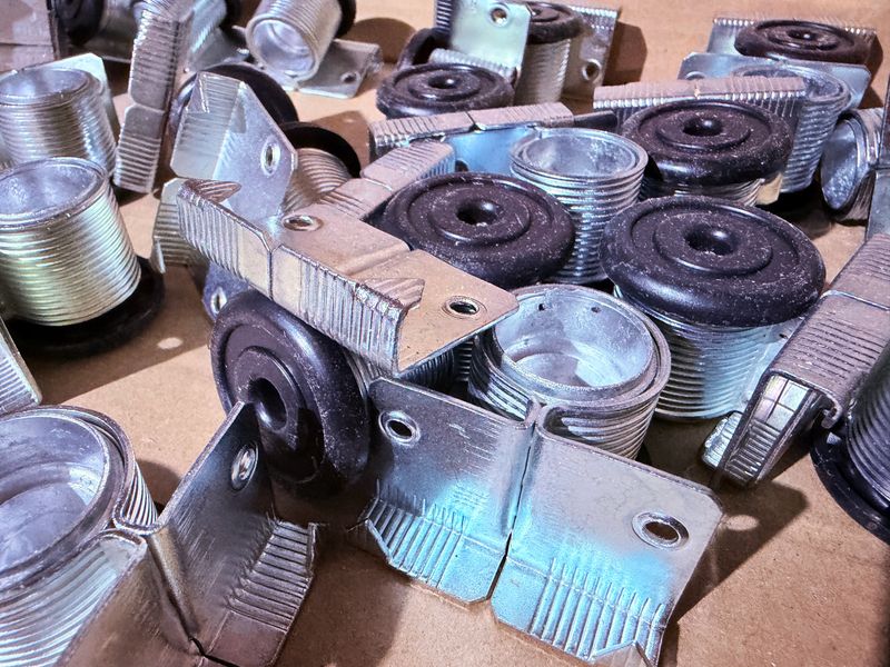 A collection of adjustable furniture supports (legs, feet, mounts) with threaded metal bases and black rubber caps. Shot from a top-down angle, highlighting metallic texture and design details.