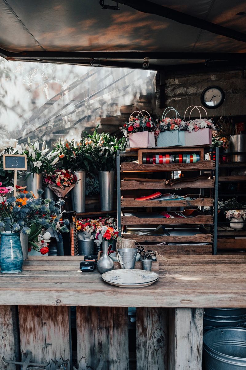 Cozy and authentic rustic flower shop counter with dried lavender and vintage gardening tools. An intimate workshop scene showing a hand tying a flower bouquet on a weathered wooden table with antique accessories. High quality photo