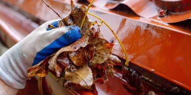 Technician hand-cleaning leaves and debris from a gutter before gutter guard installation