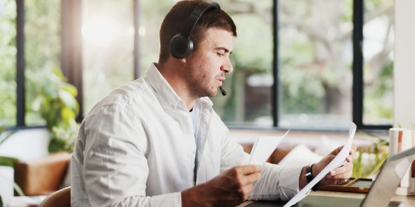 Man wearing headset, reviewing documents at desk.