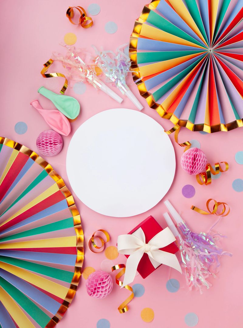 Top view flat lay of birthday party elements on soft pink background with gift box, ribbons, balloons, confetti and festive decorations