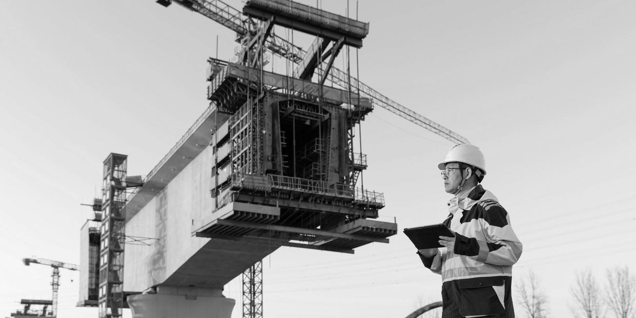 Construction engineer inspects a bridge under construction with a tablet in hand.