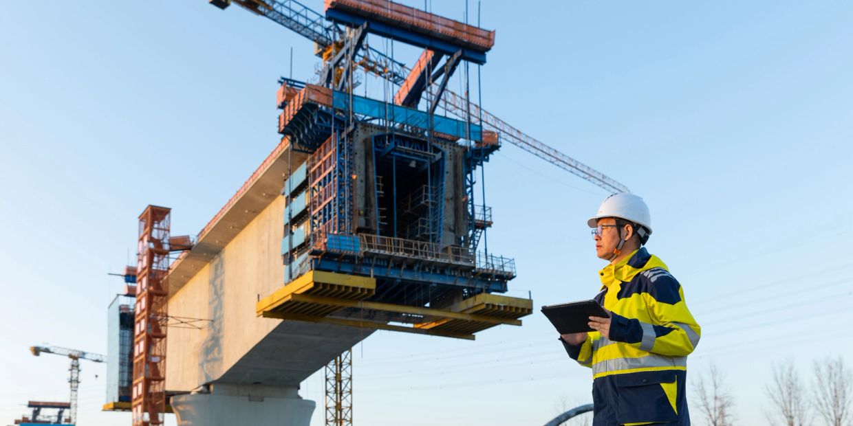 Construction engineer inspects a bridge under construction with a tablet in hand.