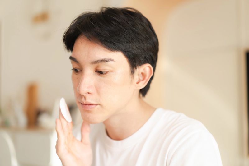 Close-up of a man using a cotton pad with cleansing liquid to clean his skin at home