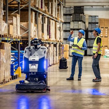 Workers in a warehouse supervising a robot.
