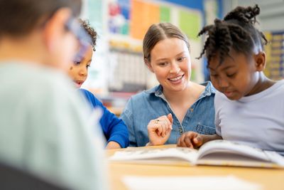 Teacher helping kids read a book in class.