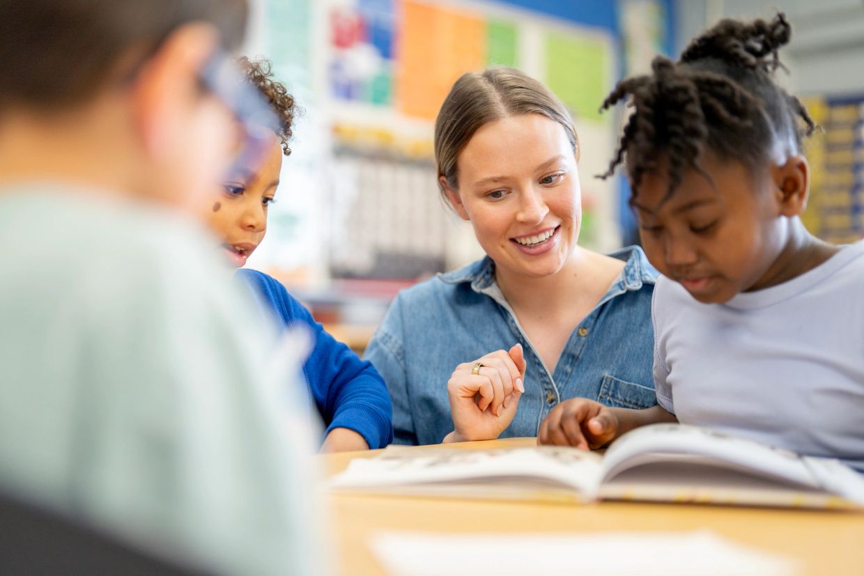 Teacher engaging with young students while reading a book together.