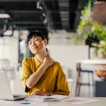 Woman experiencing neck pain while working at a desk.