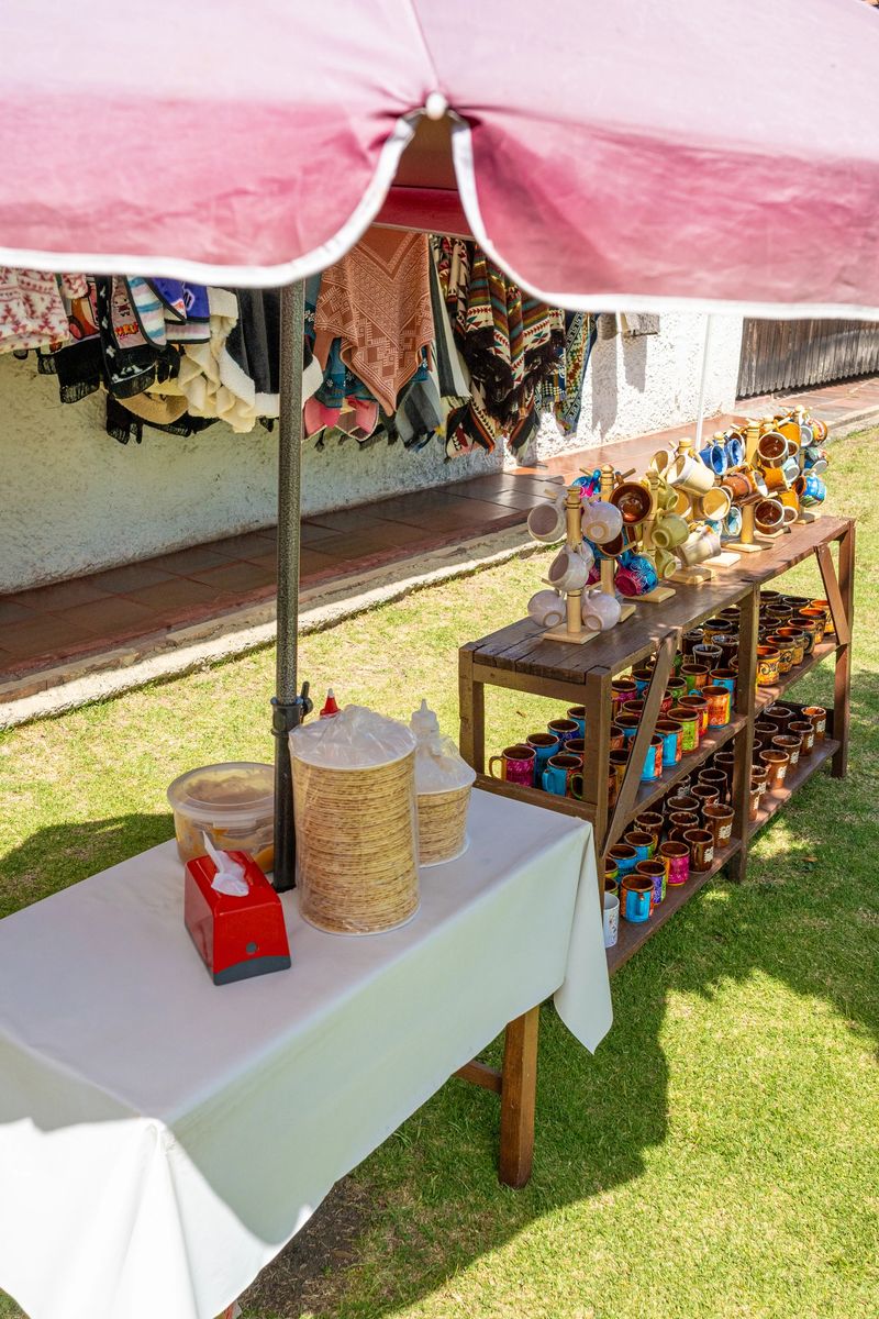 Outdoor artisan market stall and street food stall displaying colorful handmade ceramic mugs, evoking a vibrant craft market scene.
