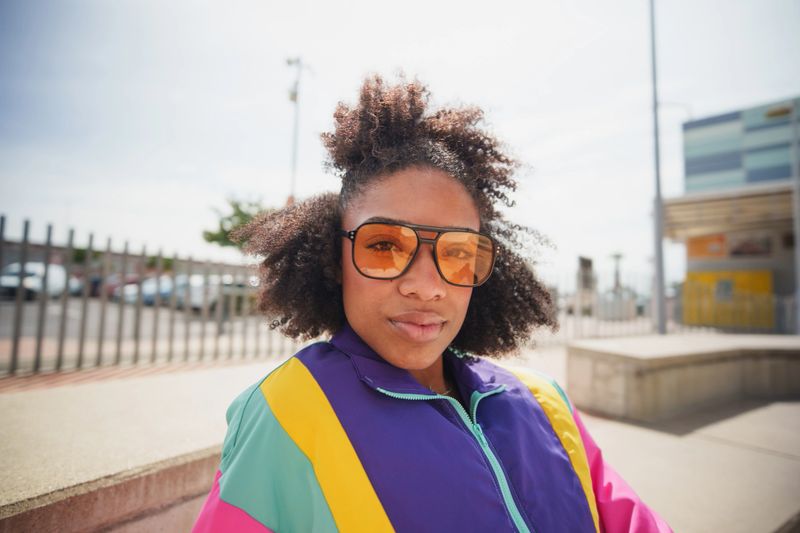 Young adult woman wearing 90s style track jacket and sunglasses in urban setting