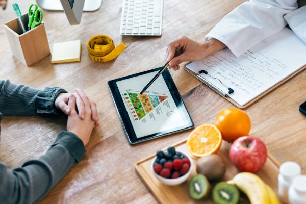 Dietitian consulting patient using tablet with food pyramid.