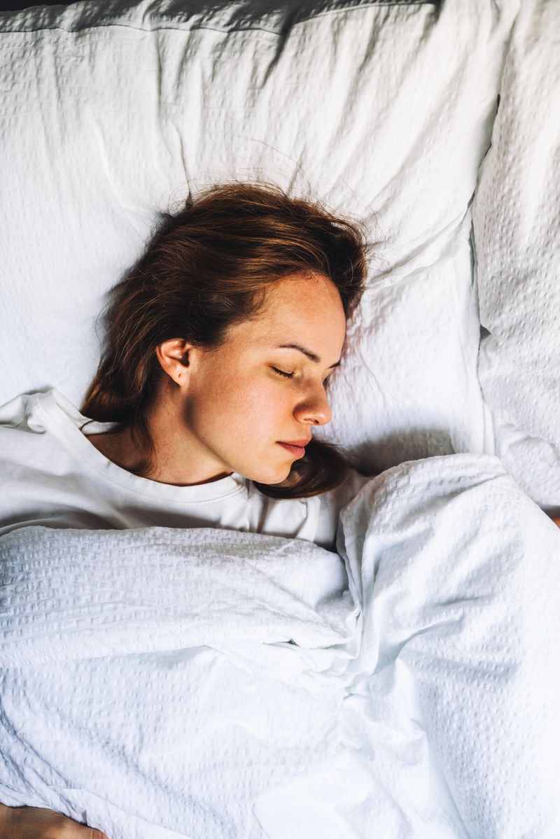 Pure comfort and morning serenity: a serene woman sleeping in a comfortable white bed.
