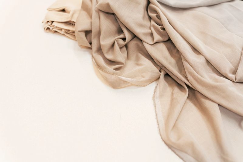 Beige fabric and lightweight textiles draped in soft folds on a work surface at a sewing workshop in an industrial building in Sweden, evoking craftsmanship, calm, and material texture.
