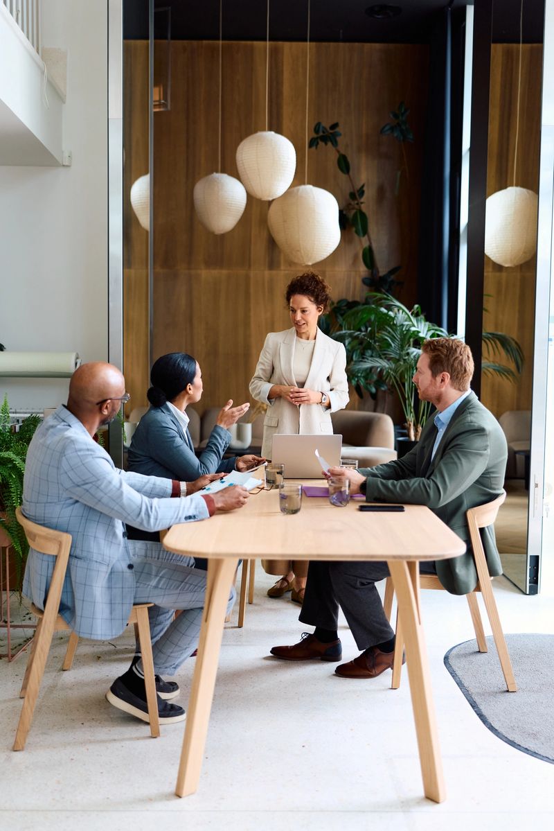 Diverse group of business professionals discussing strategy and collaborating during a corporate meeting, with a female leader presenting using a laptop in a contemporary office space