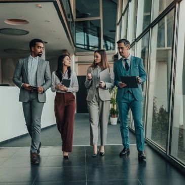 Four professionals walking and discussing in an office corridor.