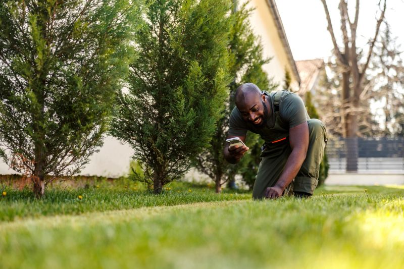 Smiling male gardener inspecting the fresh green lawn in a vibrant residential garden while using a mobile phone, representing professional landscaping and modern technology in property maintenance