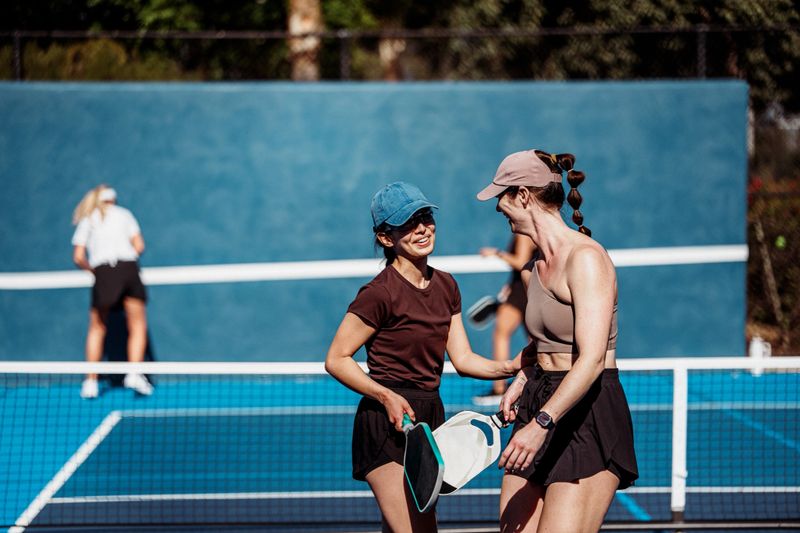 Two female pickleball teammates smile and talk on the court while preparing for an upcoming tournament match in Loma Linda, California.