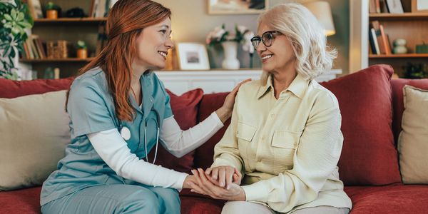 Nurse comforting an elderly woman on a couch.
