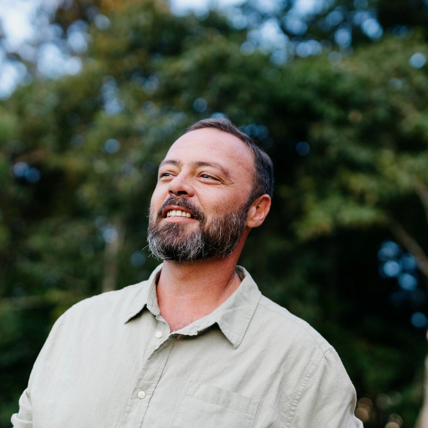 Man smiling calmly outdoors among trees