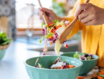 Person serving fresh salad into a bowl.