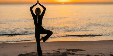 Person practicing yoga on the beach at sunset.