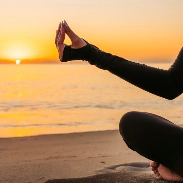 Person meditating by the beach at sunset.