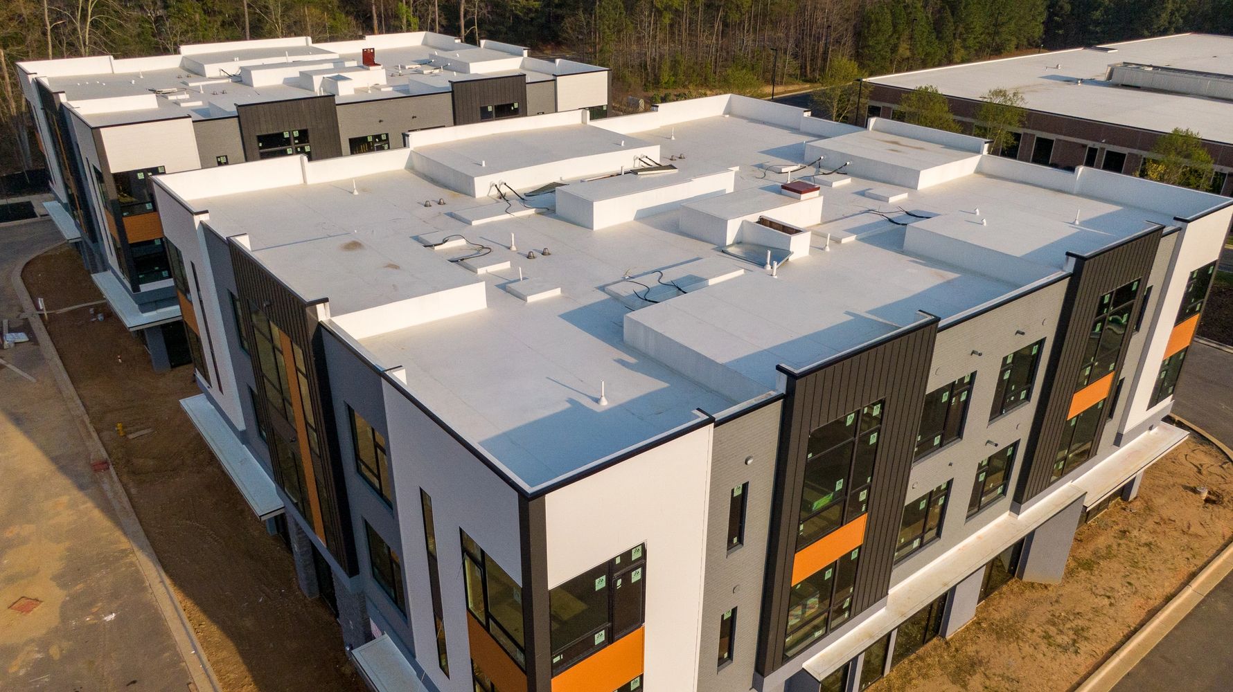 Modern commercial buildings with flat white roofs in a wooded area.