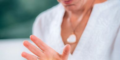 A person with a white shirt and a heart-shaped pendant raising their hand.
