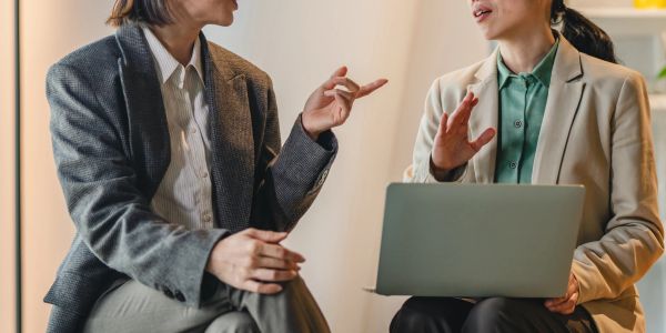 Two women in business attire discussing with a laptop.