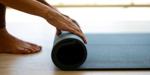 Person rolling up a black yoga mat on wooden floor.