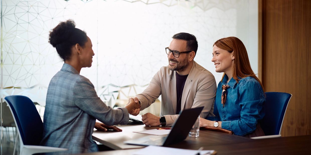 Two women and one man shaking hands in a professional setting.