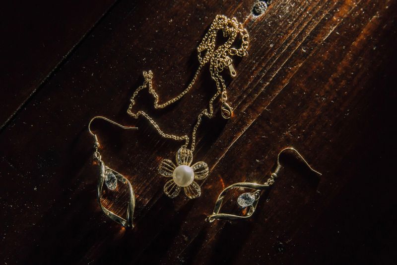 A gold necklace and earrings are displayed on a wooden table. The earrings are shaped like flowers and the necklace is made of gold