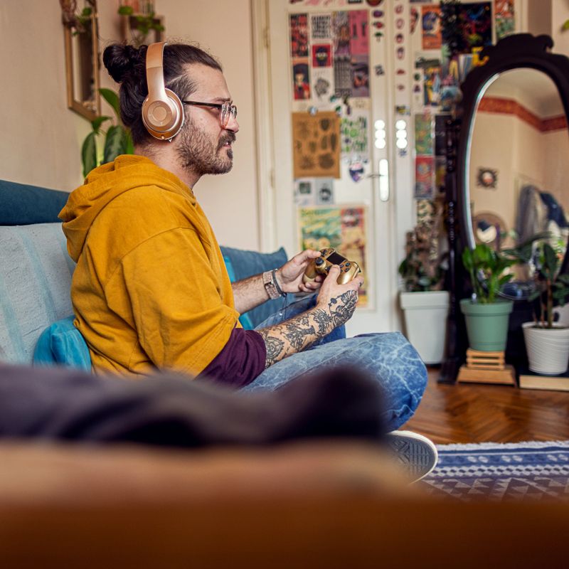 Lifestyle photo of man in a relaxing living room is focused on playing a video game with a joystick and headphones on his head.