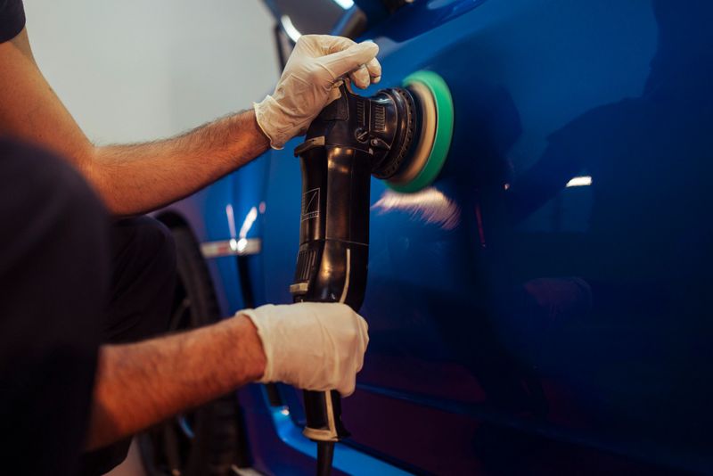 Person's hands with gloves using orbital polisher tool on a blue car, restoring shine to automotive paint finish