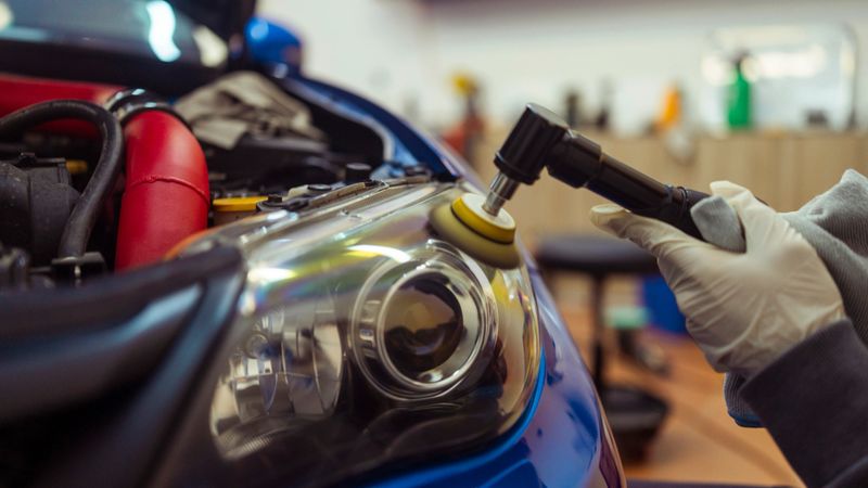 Auto mechanic polishing a car headlight with a buffer, removing oxidation and restoring optical clarity for vehicle maintenance