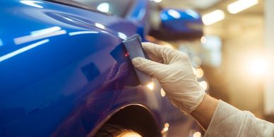 Hand wearing glove polishing a blue car's surface in a workshop.